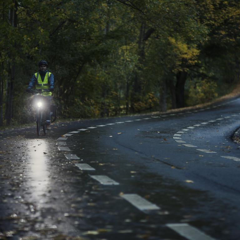 Kuvassa pyöräilijä pimeällä tiellä ajaa etuvalo palaen.